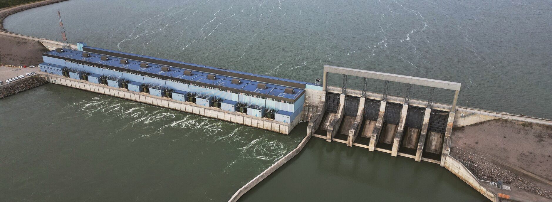 An aerial view of a hydroelectric generating station and spillway on a northern river.